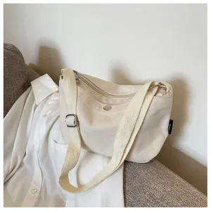 Detail of minimalist cream canvas crossbody bag with silver zipper and shoulder strap