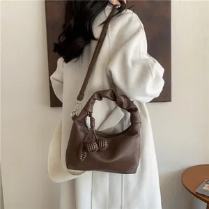 Brown half-moon shoulder bag with ruched handle and knot details on a beige backdrop