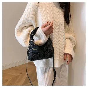 Détail du sac à main tissé noir en cuir avec anses torsadées et chaîne dorée sur pull crème