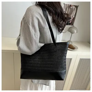 Detalle de bolso tote de paja negra con base de cuero y correas delgadas al hombro