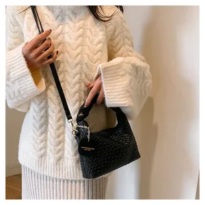 Gros plan d'un sac à main tissé noir avec boucle dorée sur un pull blanc en maille épaisse