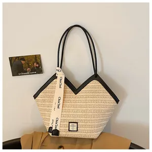Detail of the woven straw tote bag featuring black leather straps and a decorative ribbon