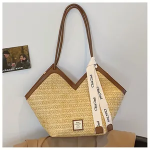 Close-up of woven straw tote bag with brown leather handles and decorative ribbon detail