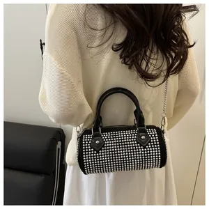 Detail of a black punk-style cylinder bag with silver studs and chain strap worn by a model
