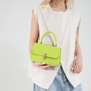 Lime green structured leather handbag with gold lock shown with beige top and denim skirt