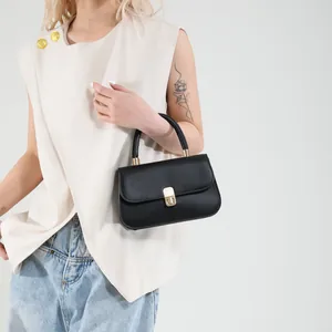 Minimalist black matte leather handbag with gold clasp carried by a model in casual outfit