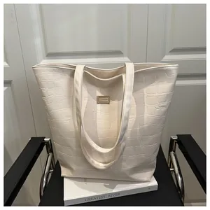 Macro detail of creamy white crocodile embossed leather tote bag with gold logo plaque