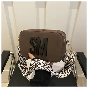 Close-up of brown camera bag with SM logo and geometric wide woven shoulder strap