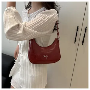 Rote Schultertasche mit Krokodilprägung und silberner Schleife am Model getragen