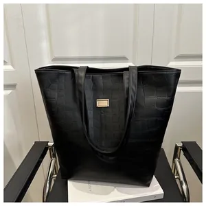 Close-up of large black croc-effect tote bag with gold logo plate on a black chair