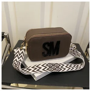Close-up of brown suede camera bag with SM logo and geometric wide shoulder strap