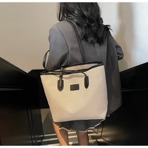 Close-up of beige canvas tote bag with black leather trim and decorative patch on side