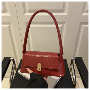 Détail d'un sac porté épaule rouge effet crocodile avec un fermoir doré rectangulaire