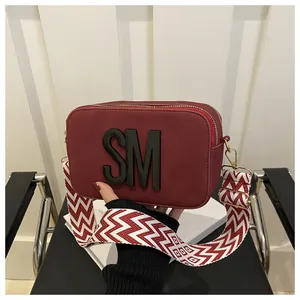 Detail of burgundy camera bag with SM logo and wide red-white herringbone strap