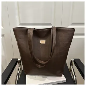 Detail of dark brown faux crocodile leather tote bag with a golden metal buckle