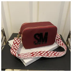 Close-up of burgundy camera bag with SM letters, dual zippers and wide patterned strap
