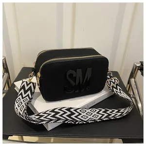 Detail of black camera bag with 3D letters and geometric pattern woven wide strap
