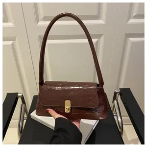 Détail de la texture croco marron foncé et du fermoir métallique doré sur le sac à main