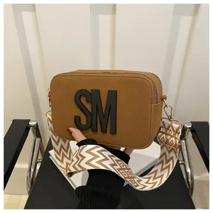 Detail of brown suede camera bag with black SM logo and wide geometric shoulder strap