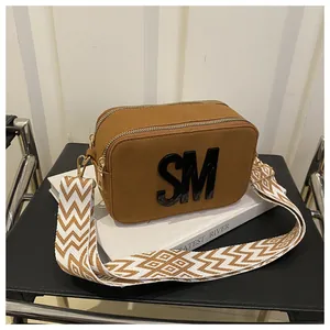 Macro detail of brown suede crossbody camera bag with 3D letters and gold zippers