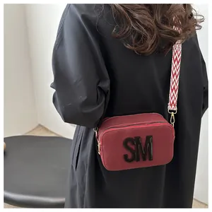 Close-up of burgundy canvas camera bag with SM patch and patterned wide strap