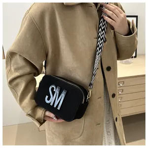 Detail of black crossbody camera bag featuring silver SM logo and patterned shoulder strap