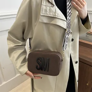 Brown camera crossbody bag with wide geometric strap and 3D SM logo for daily use