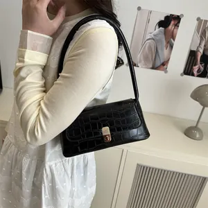 Sac sous le bras noir à motif crocodile et boucle dorée porté par un mannequin chic