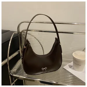 Detail of chocolate hobo bag featuring a silver metal bow and slim shoulder strap