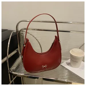 Detail view of burgundy crescent shoulder bag with silver bow ornament on a shelf