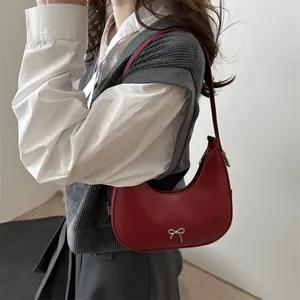Deep red half-moon shoulder bag with silver metal bow worn by a model in a minimal setting