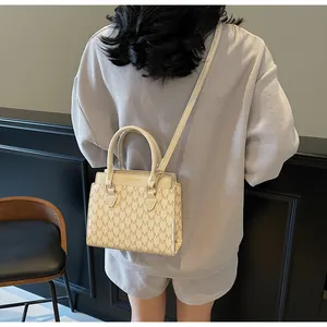 Detail of elegant beige tote bag with M letter pattern carried by a model in a grey suit