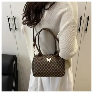 Dettaglio di una borsa a cilindro vintage marrone con motivi geometrici e ciondolo a farfalla