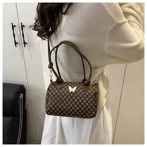 Dettaglio della borsa cilindrica marrone vintage con ornamento a farfalla bianca e motivo geometrico