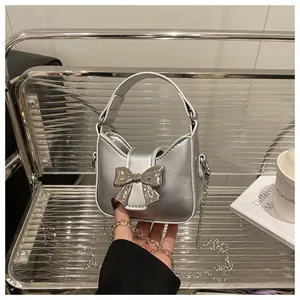 Détail du mini sac argenté avec nœud et bandoulière chaîne sur une chaise moderne