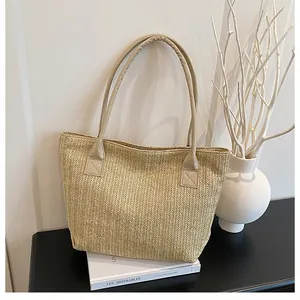 Dettaglio della borsa tote in paglia intrecciata con trama beige e manici in pelle crema