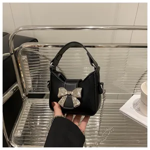 Détail d'un mini sac à main noir avec un grand nœud en métal argenté et une bandoulière