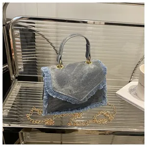Detail of blue denim crossbody bag with fringe trim and golden metal chain strap