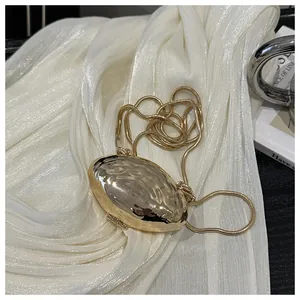 Detail of golden shell-shaped clutch showing hammered metal texture and snake chain