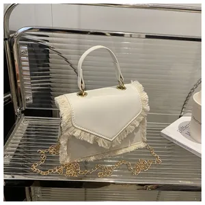 Detailed shot of cream small square bag featuring fringe edges and gold chain strap
