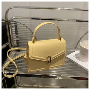 Detail of pale yellow crossbody bag with gold oval twist lock and decorative stitching