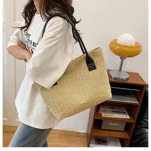 Dettaglio borsa tote in paglia intrecciata con spalline in pelle nera su modella casual