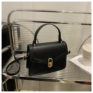Detail of a black square crossbody bag with a golden oval twist lock and a top handle