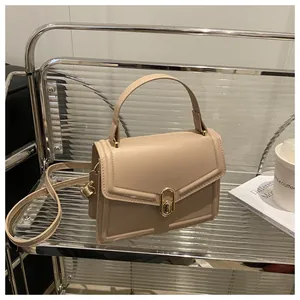 Detail view of the beige small square bag with golden lock on an acrylic chair