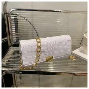Detail of white crocodile embossed texture with gold chain strap on a modern square bag