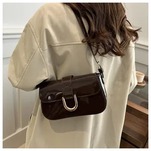 Detail of dark brown patent leather shoulder bag with gold U-shaped hardware buckle