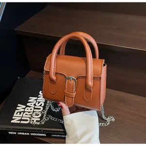 Dettaglio di una mini borsa a mano marrone caramello con catena in metallo e fibbia vintage