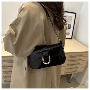 Glossy black patent leather underarm bag with gold D-ring buckle shown on shoulder