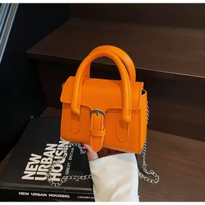Dettaglio mini borsa arancione con fibbia metallica e catena argentata su libri di moda