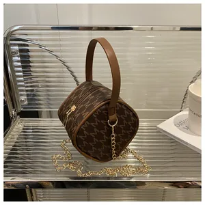 Detail of a brown cylindrical mini bag with M-pattern and gold metal chain strap